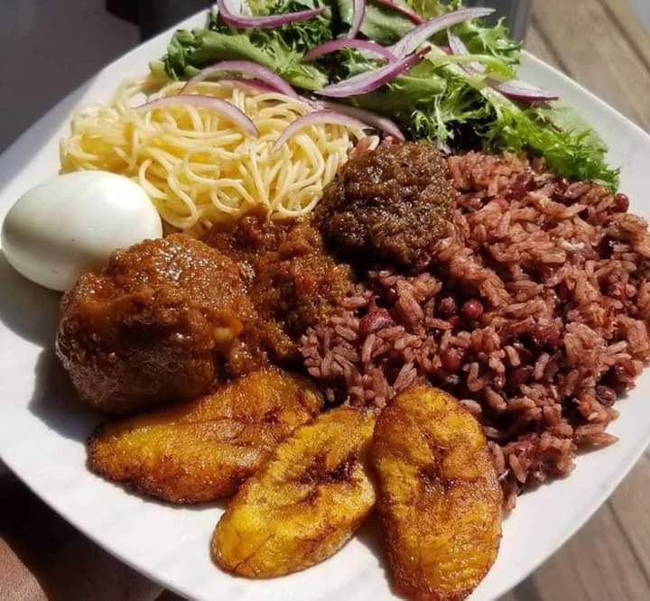 Rice and beans served with colourful vegetables, egg, fish and golden fried plantain.